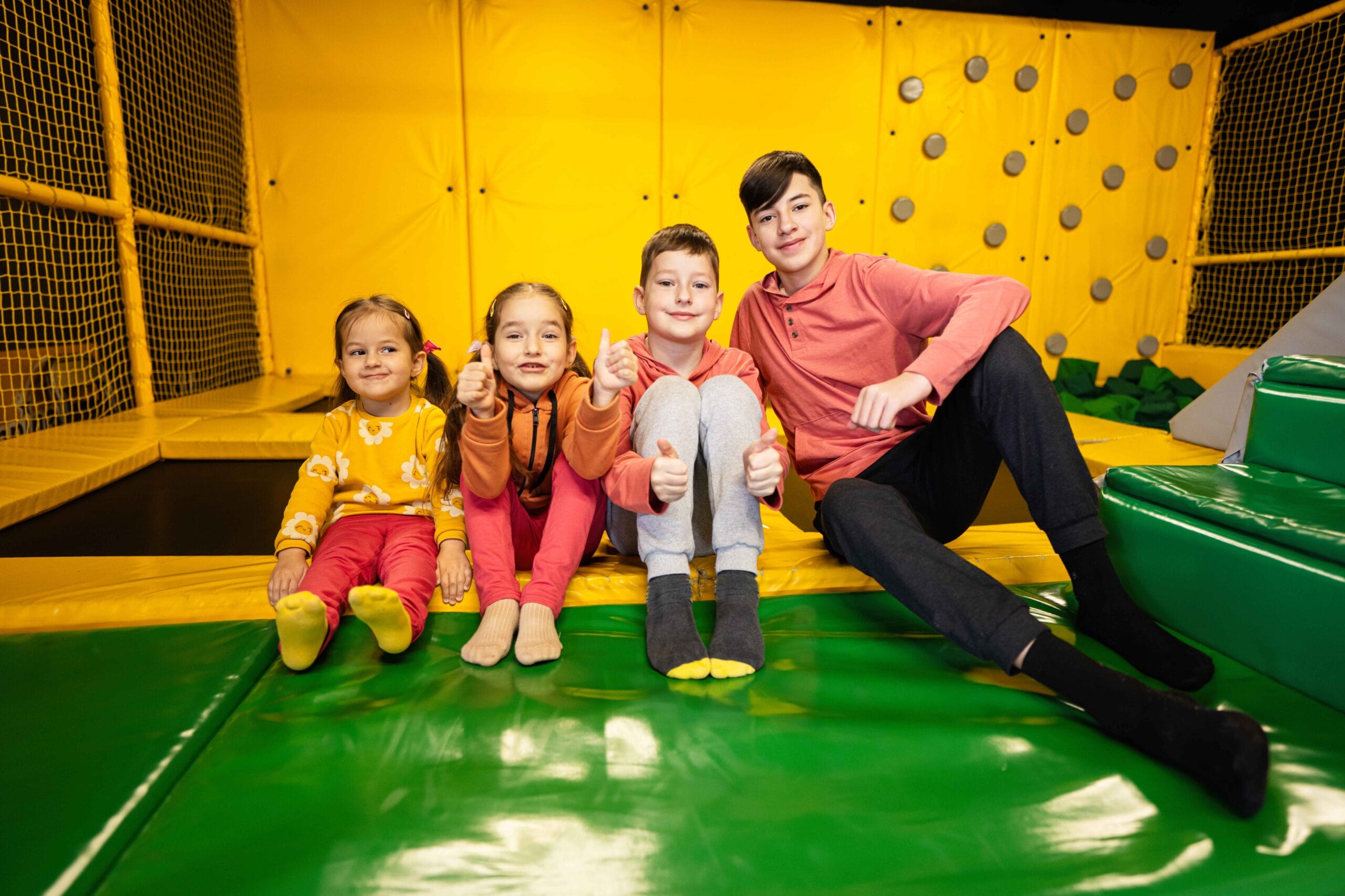 Group of children sitting on a trampoline, giving thumbs up.